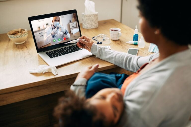 Close-up of black family doctor having video call with a mother who is measuring daughter's temperature at home during coronavirus pandemic.