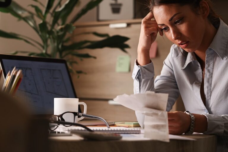 Businesswoman feeling worried about financial debts and analyzing bills while working in the office.
