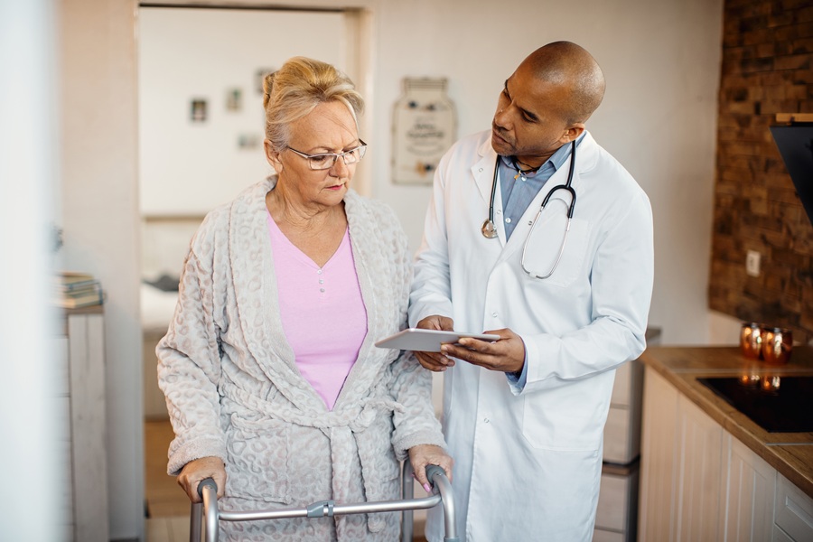 Black doctor showing something on digital tablet to senior woman who is using mobility walker at nursing home.